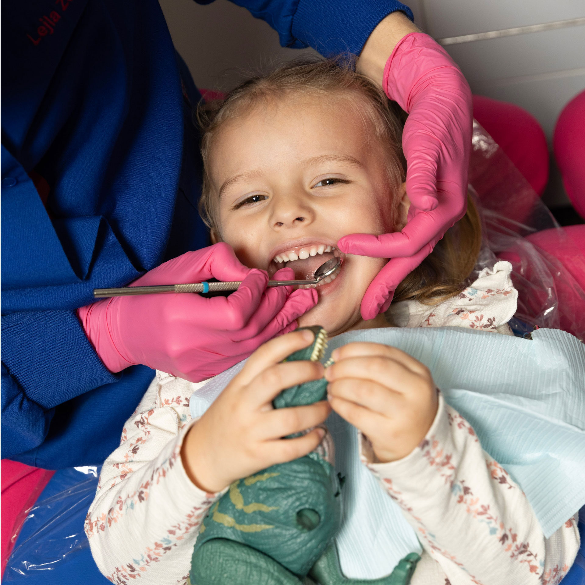 close up of dentist holding dental mirror to look in young patient's mouth who is smiling at the camera during dental exam